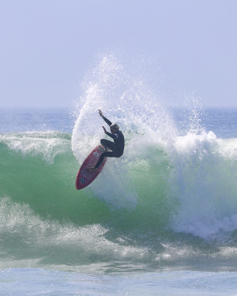 Surfer on his Red Tiger Pyzel, snapping painting the summery blue sky with white water spray