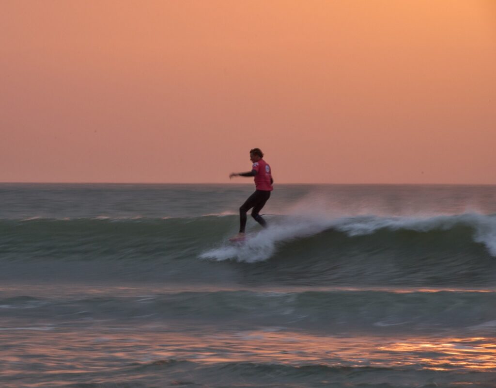 Surfer glides effortlessly on a groovy longboard, while the sun sets in a vibrant orange